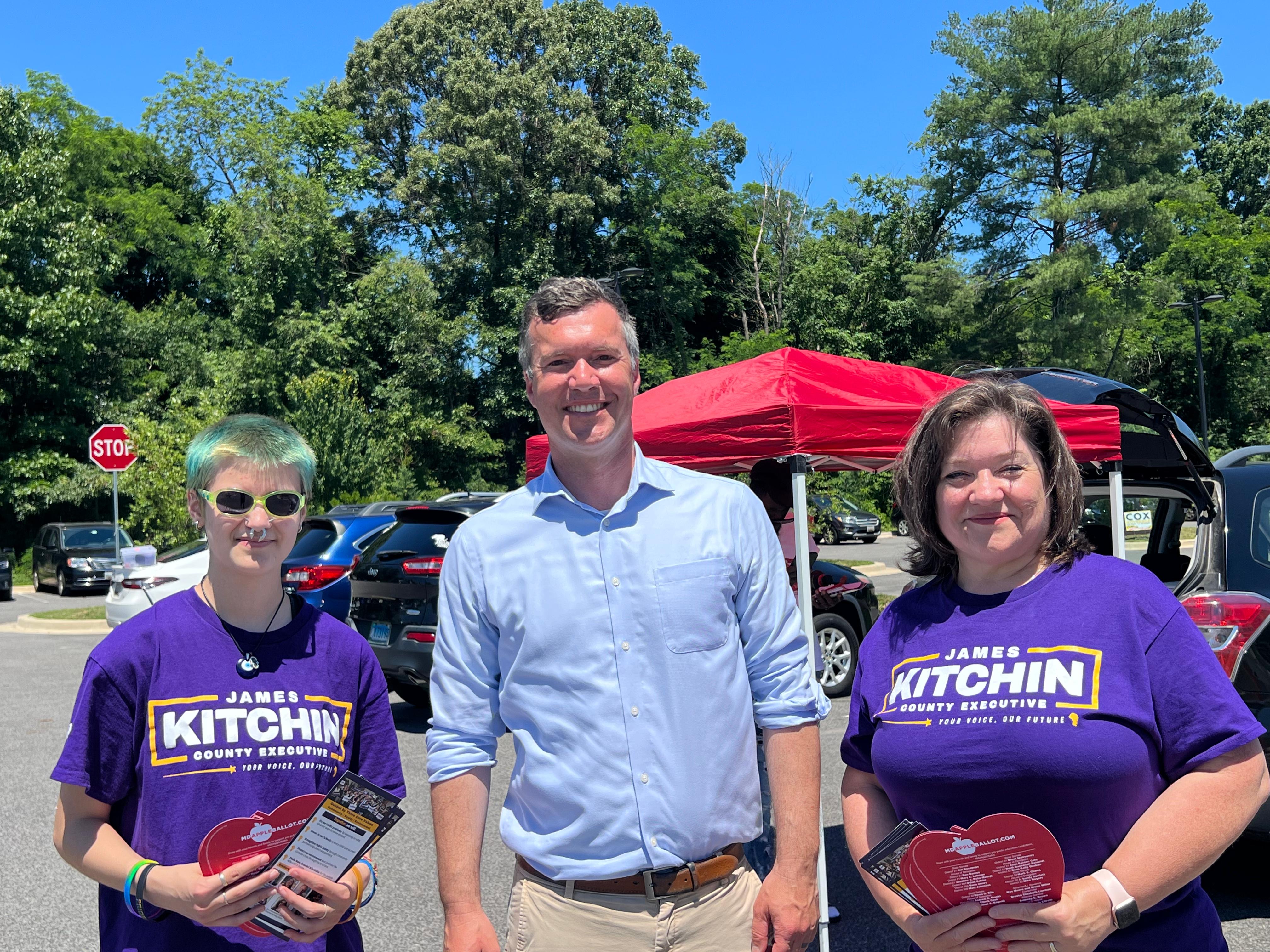 Two volunteers in Kitchin purple shirts flanking James at an Early Voting location